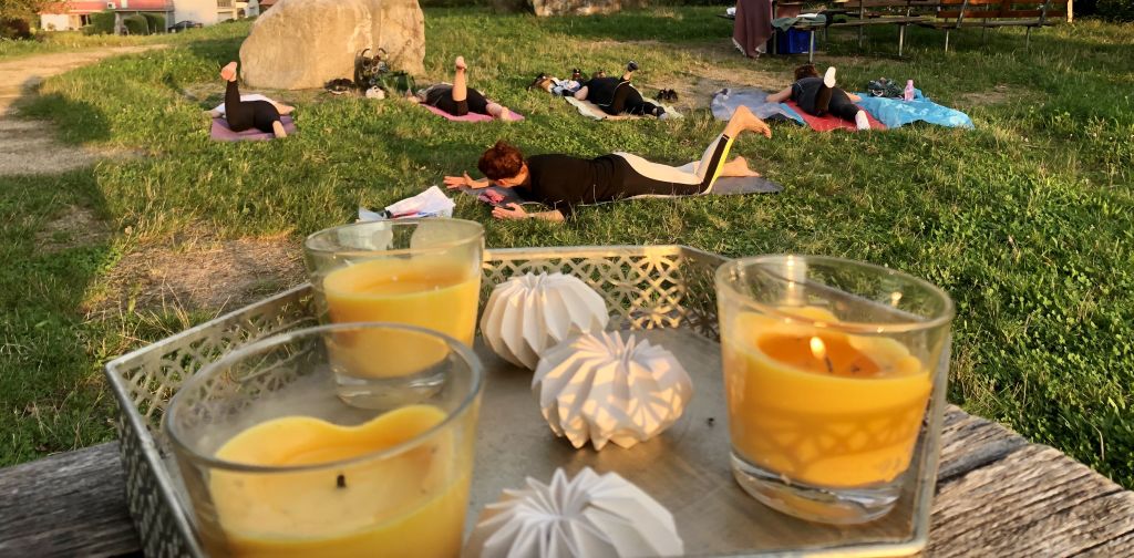 Mehrere Personen üben Pilates auf einer Wiese. Im Vordergrund stehen Kerzen